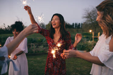 Multi-ethnic group of friends enjoying party with sparklers. Women having fun with sparklers outdoors in evening. - JLPSF26001