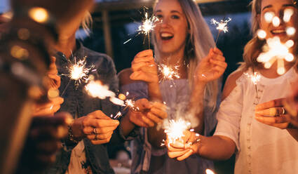 People at night holding sparklers. Group of friends enjoying with sparklers in evening. - JLPSF26003