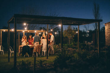 Männer und Frauen stehen um einen Tisch in einem Gartenrestaurant. - JLPSF26006