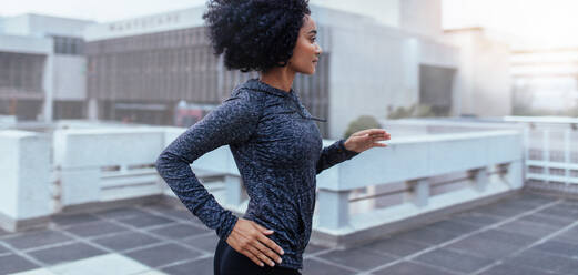 Young woman running early in the morning. Female athlete in sweatshirt jogging in city with buildings all around in the background. - JLPSF26008