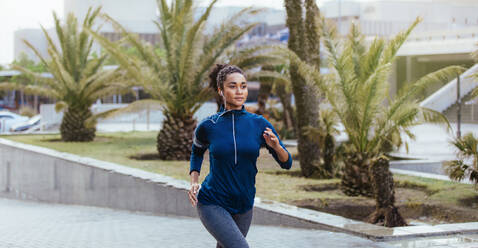 Läuferin im Jogging-Outfit, die auf einer Straße läuft. Frau hört Musik mit Kopfhörern beim Laufen. - JLPSF26016