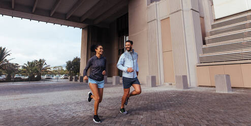 Sportler unterhalten sich während ihres morgendlichen Laufs. Mann und Frau im Jogging-Outfit laufen morgens im Freien. - JLPSF26017