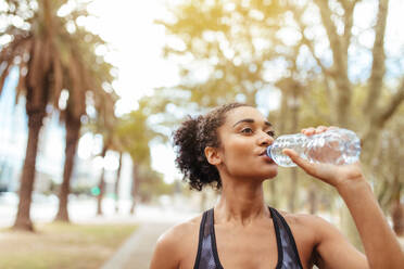 Eine Läuferin trinkt während des Trainings Wasser aus einer Flasche. Eine Sportlerin macht eine Trainingspause. - JLPSF26028