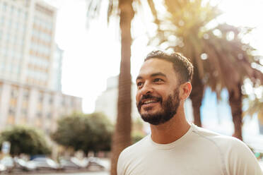 Close up of a male athlete running in city. Young man in sports shirt running outdoors with trees and buildings in the background. - JLPSF26030