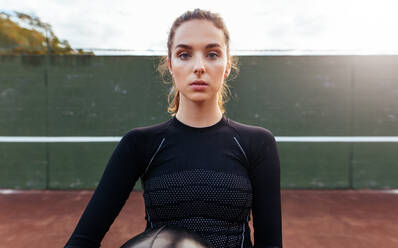 Porträt einer sportlichen jungen Frau auf dem Tennisplatz. Schöne Fitnessfrau in Sportkleidung mit Fitnessball schaut in die Kamera. - JLPSF26037