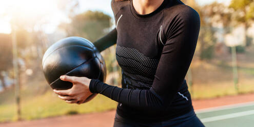 Abgeschnittene Aufnahme einer fitten jungen Frau, die mit einem Medizinball trainiert. Nahaufnahme einer Sportlerin, die mit einem Fitnessball im Freien auf einem Tennisplatz trainiert. - JLPSF26038