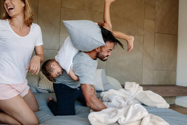 Familie spielt zusammen auf dem Bett zu Hause. Kleiner Junge spielt mit seinen Eltern im Schlafzimmer. - JLPSF26053