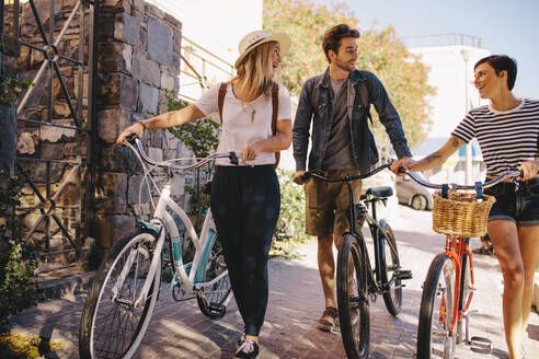 Drei junge Freunde, die zusammen spazieren gehen und Spaß haben. Junge Leute mit Fahrrädern, die draußen in der Stadt spazieren gehen. - JLPSF26055