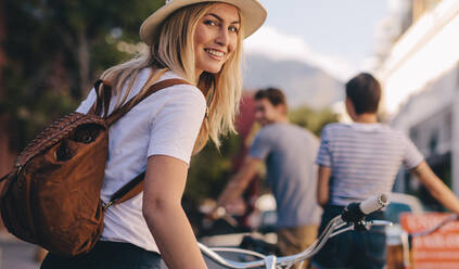 Rear view of beautiful woman walking with her bicycle and friends in background. Female with her bike looking back. - JLPSF26056