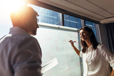 Geschäftsfrau schreibt während einer Diskussion im Sitzungssaal Ideen auf ein Whiteboard. Zwei Kollegen diskutieren im Büro über Geschäftsideen. - JLPSF26065