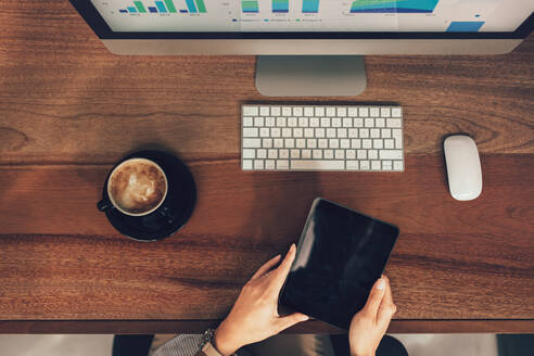 Top view of female hands holding digital tablet while sitting at her desk. Cropped shot of female business professional working with tablet computer in office. - JLPSF26071