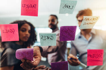 Geschäftsleute schreiben auf Haftnotizen und kleben sie auf Glas im Büro. Bunte Post-it-Notizen auf Glas mit Notizen auf sie. - JLPSF26073