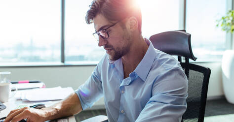 Closeup of businessman sitting at his desk in office. Man wearing spectacles sitting at his work station looking down at his desk. - JLPSF26079