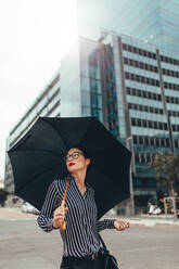 Asian businesswoman on city street with umbrella. Female business professional with umbrella walking down city street. - JLPSF26084