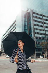 Asiatische Geschäftsfrau auf der Straße mit Regenschirm. Weibliche Geschäftsfrau mit Regenschirm zu Fuß auf der Straße. - JLPSF26084