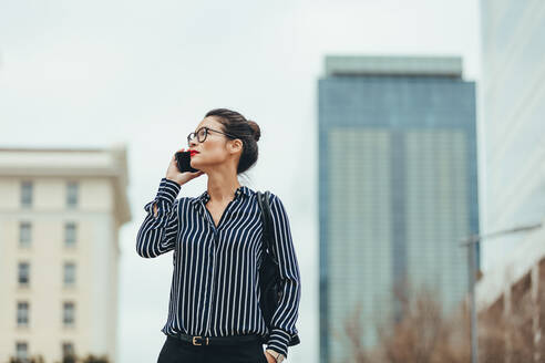 Junge asiatische Geschäftsfrau, die im Freien spazieren geht und mit einem Handy spricht. Weibliche Geschäftsfrau, die im Freien spazieren geht und ein Handy benutzt. - JLPSF26090
