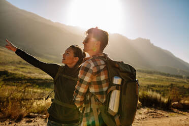 Young man and woman on a hike. Young couple with backpack hiking in nature, with woman pointing away. - JLPSF26110