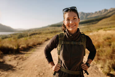 Porträt einer lächelnden jungen Frau mit Rucksack auf einer Landpartie. Asiatische Wanderin auf einem Wanderweg in einem Naturschutzgebiet. - JLPSF26111