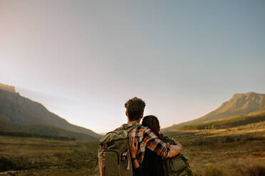 Young tourists with backpacks enjoying valley view. Rear view of young man and woman on hiking trip standing together and admiring the beautiful landscape - JLPSF26116