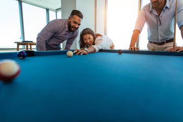 Junge Männer und Frauen machen eine Pause von der Arbeit. Eine Geschäftsfrau spielt im Büro Billard, während ihre Kollegen zusehen. - JLPSF26126