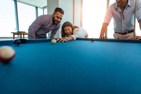 Junge Männer und Frauen machen eine Pause von der Arbeit. Eine Geschäftsfrau spielt im Büro Billard, während ihre Kollegen zusehen. - JLPSF26126