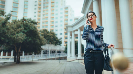 Businesswoman walking outdoors and talking on mobile phone. Asian female walking outside using mobile phone. - JLPSF26130