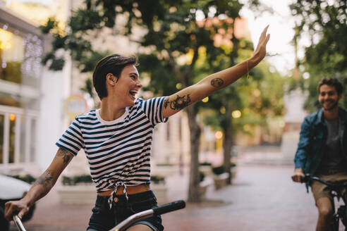 Eine Frau fährt Fahrrad und winkt einem männlichen Freund zu. Ein Paar genießt es, durch die Stadt zu radeln. - JLPSF26131