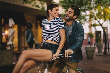 Schöne junge Frau sitzt auf dem Fahrradlenker ihres Freundes und lächelt. Romantisches Paar auf einem Fahrrad in der Stadt. - JLPSF26133