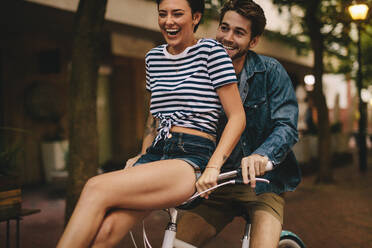 Man riding bicycle with his girlfriend sitting on handlebar. Couple having fun while riding bicycle. - JLPSF26134