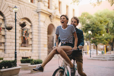 Couple enjoying on a bicycle in the city. Cheerful woman sitting on handlebar of boyfriends bicycle. - JLPSF26138