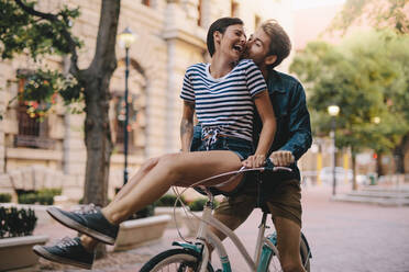 Laughing woman sitting on boyfriends bicycle handlebar. Cheerful couple on a bike together in the city having fun. - JLPSF26139