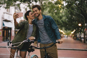 Romantic couple with bicycles taking selfie. Women taking selfie and kissing her boyfriends cheek. - JLPSF26140