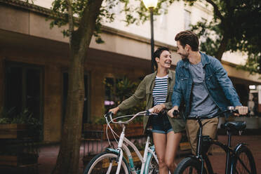 Happy man and woman walking on a street with their bikes. Young couple with bicycles on the city street. - JLPSF26142