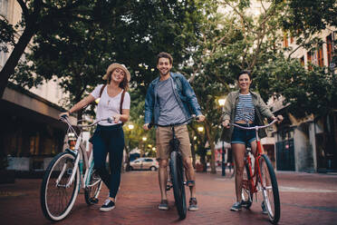 Drei junge Leute mit ihren Fahrrädern in voller Länge auf einer Stadtstraße. Freunde auf Fahrradtour durch die Stadt. - JLPSF26154