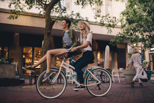 Lächelnde Frau sitzt mit ihrer Freundin auf dem Fahrradlenker. Schöne Frauen genießen auf dem Fahrrad in der Stadt. - JLPSF26155