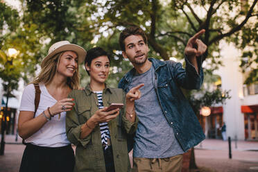 Eine Gruppe von Freunden auf einer Stadttour, die ihr Handy zur Navigation benutzen. Drei junge Leute erkunden eine Stadt mit Hilfe von Smartphone-GPS. - JLPSF26157