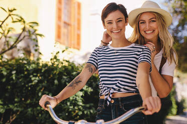 Smiling women cycling with her friend on city street. Two young females riding together on a bicycle outdoors and having fun. - JLPSF26158