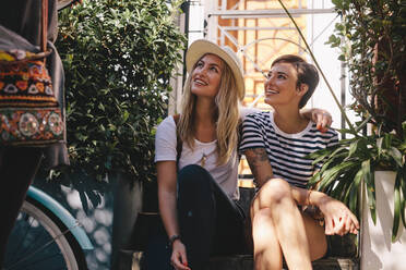 Two young woman sitting outdoors and looking away. Female friends relaxing by the street. - JLPSF26164