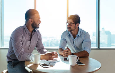 Business executives discussing work in office. Two businessmen sitting on a round table and discussing business matters. - JLPSF26166