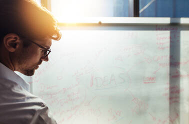 Businessman writing his ideas on whiteboard in office. Close-up of businessman wearing glasses presenting a business plan. - JLPSF26173