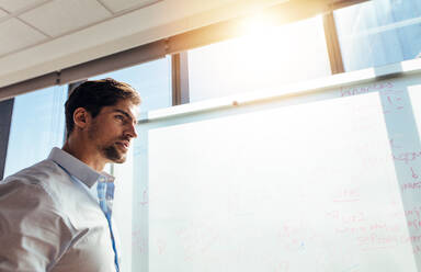 Closeup of businessman against whiteboard in office. Young entrepreneur writing ideas on whiteboard. - JLPSF26179