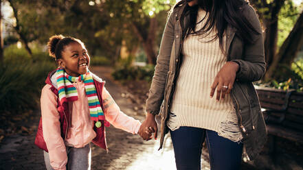 Niedliches kleines glückliches Mädchen, das die Hand einer Frau hält und im Freien spazieren geht. Mutter und Tochter spazieren im Freien und lächeln. - JLPSF26183