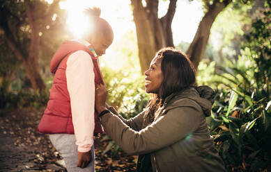 Seitenansicht einer afrikanischen Frau mit ihrer Tochter, die an einem sonnigen Tag im Freien lächelt. Mutter und Tochter sehen sich an und lächeln. - JLPSF26184