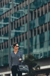 Asiatische Geschäftsfrau vor einem Bürogebäude. Geschäftsfrau mit Handtasche auf der Straße in der Stadt. - JLPSF26200