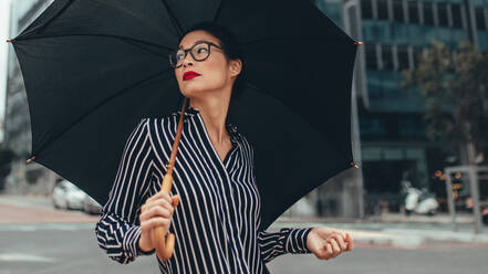 Junge Business-Frau zu Fuß auf der Straße mit Regenschirm. Asiatische weibliche Business-Profi mit Regenschirm zu Fuß nach unten Stadt Straße. - JLPSF26205