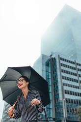 Urbane Frau lächelnd auf der Stadtstraße mit Regenschirm. Geschäftsfrau im Freien in der Stadt hält Regenschirm und lächelnd. - JLPSF26208
