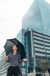 Junge Geschäftsfrau auf der Straße mit Regenschirm. Asiatische Geschäftsfrau mit Regenschirm zu Fuß auf der Straße. - JLPSF26211