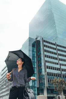 Young businesswoman on city street with umbrella. Asian female business professional with umbrella walking down city street. - JLPSF26211