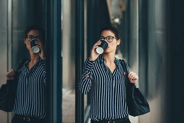 Junge Frau vor dem Geschäftszentrum beim Kaffeetrinken. Asiatische Geschäftsfrau beim Kaffee trinken im Freien. - JLPSF26220