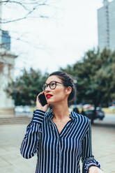 Asian businesswoman walking outside using mobile phone. Female business professional outdoors on city street talking on mobile phone. - JLPSF26224